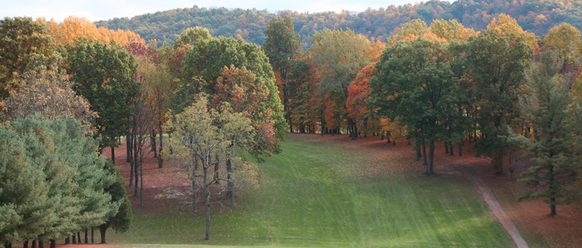 Wide fairway lined with autumn-colored trees and hills in the background, orange and green tones, scenic fall mood
